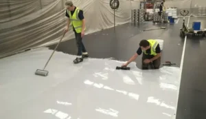 Contractors applying a self-leveling, durable epoxy coating to a warehouse floor.