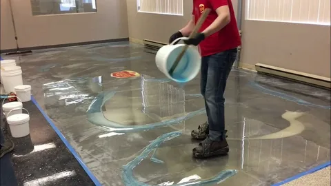Person pouring blue and metallic epoxy resin onto a concrete floor to create a custom decorative, flowing, artistic finish.